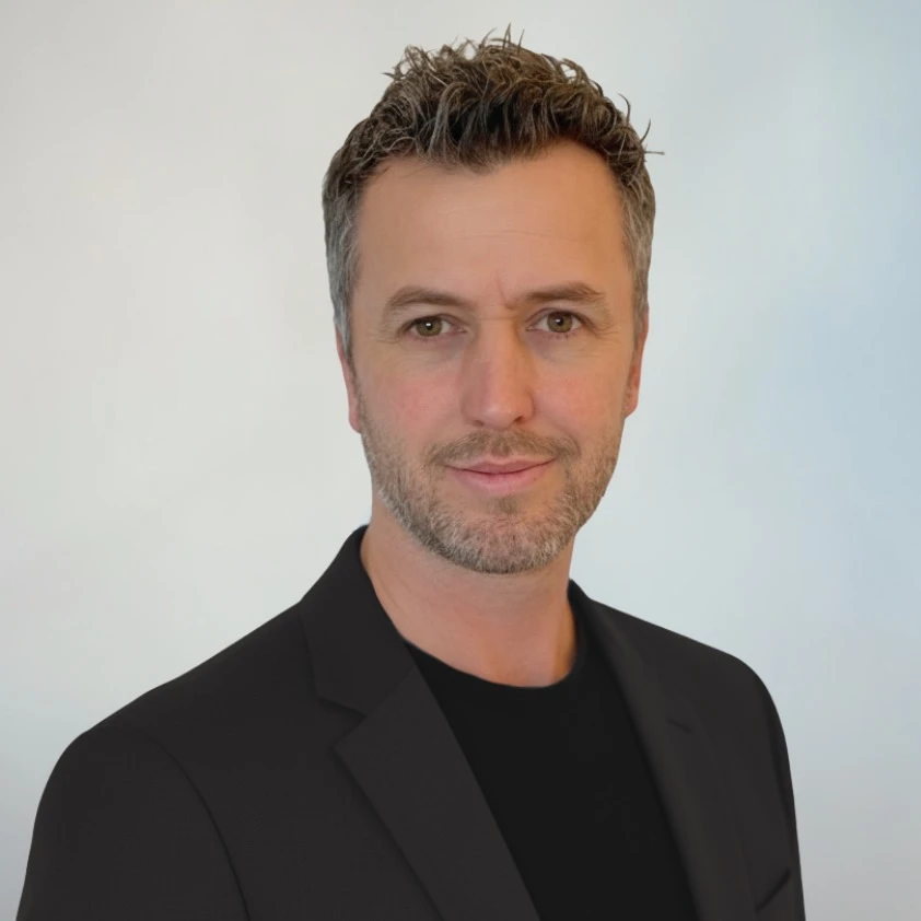Professional headshot of Kieran Doyle, smiling and wearing business attire against a neutral background.
